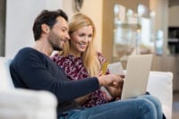 Portrait of happy couple paying bills online using laptop and credit card. Couple with computer and credit card buying online through e-commerce. Banking online.